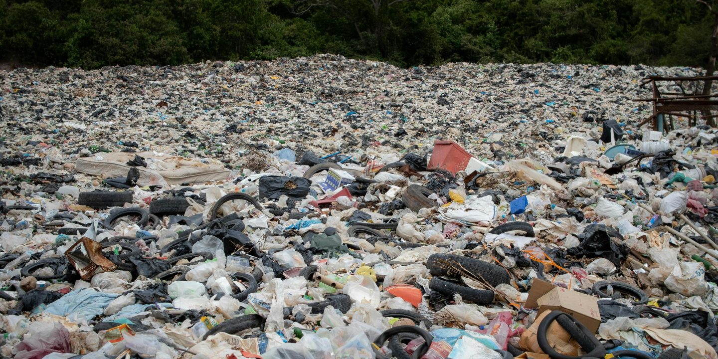 A large area filled with rubbish and old tires with a jungle in the background