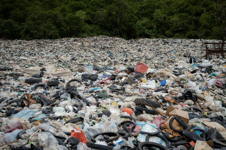 A large area filled with rubbish and old tires with a jungle in the background